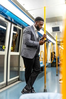 Stylish businessman using mobile phone while standing on a modern subway train, commuting to work