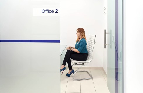 A woman sits in a modern dental clinic office, surrounded by a minimalist design. The light