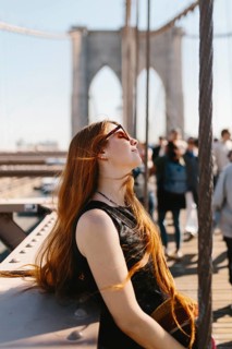 Young woman with sunglasses basks in the sun on a busy bridge in New York. Her long hair flows
