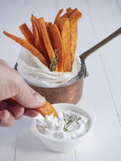 Hand dipping roasted sweet potato sticks in yoghurt sauce