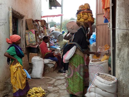 Women in colorful clothes at a market wear bananas on their heads and sell goods in alleys,