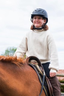 A young girl wearing a helmet is enjoying a lovely day at the farm, riding a horse and embracing