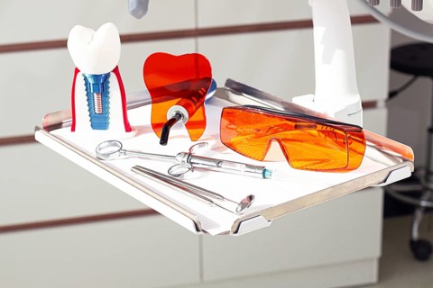 On the tray are various dental instruments, a model dental implant and bright orange safety