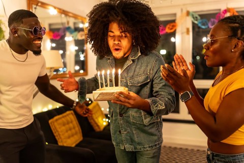 Man blowing birthday cake asking for wish next to multi-ethnic friends at home party