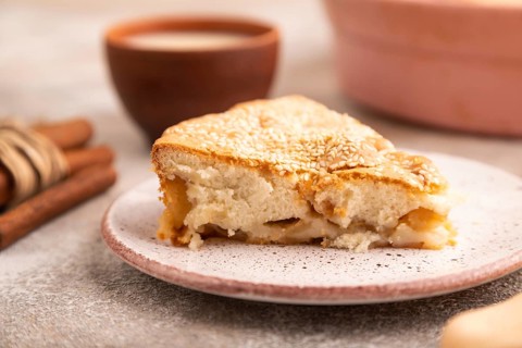 Apple Charlotte cake on brown concrete background and orange linen textile, cup of milk, side view,