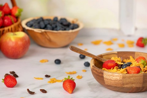 Close-up of a filled cereal bowl surrounded by ingredients, apple, strawberries, blueberries and