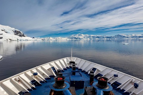 Ship on calm water in arctic landscape with snowy mountains and clouds, The landscape in the
