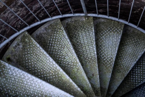Steps of old metal spiral staircase disappear in darkness