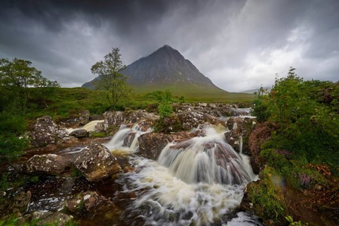 Dramatic landscape with stormy sky, wild river and strong waterfalls in front of a gloomy mountain,