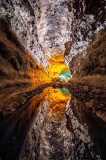 Lava tunnel, illuminated lava cave with perfect reflection in an underground lake, Cueva de los