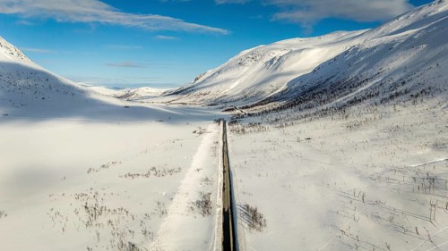 A stunning aerial view captures a winding road cutting through a vast snow-covered Nordic