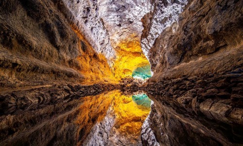 Lava tunnel, illuminated lava cave with perfect reflection in an underground lake, Cueva de los