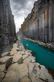 Tourist standing by the river in Stuðlagil Canyon, turquoise blue river between basalt columns,