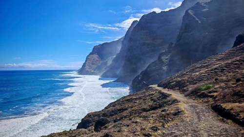 Dramatic coastline with steep cliffs and a trail along the ocean, A hiker in the distance, hiking