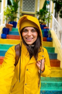 Woman smiling and enjoying urban travel, wearing a vibrant yellow rain jacket and beanie while