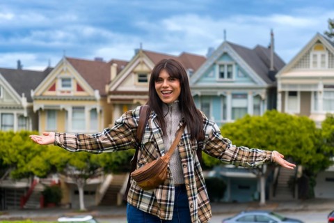 Young woman standing in front of the colorful victorian houses of alamo square park, smiling
