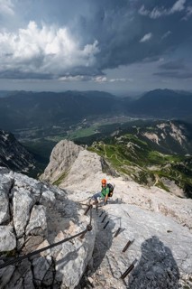 Mountaineer with helmet climbing on the rock in a secured climb, on a narrow rocky ridge, in steep