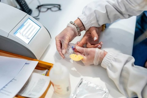Healthcare worker wearing gloves performing a rapid finger prick blood glucose test on a patient