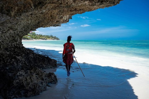 A Masai man walks along a beautiful Indian Ocean beach