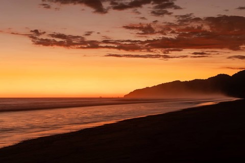 After sunset, the deep red sky glows above palms and ocean spray with views of Corcovado National