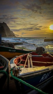 Colorful fishing boats on the shore with ropes and setting sun over the sea, dramatic coastal