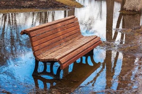 Empty brown stained long wooden sitting bench with black cast iron legs surrounded by flood water