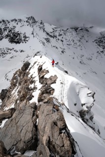 Mountaineer descending the narrow ridge of Piz Laviner, view of mountain panorama in wintry