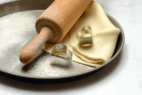 Rolled dough on cake tray with dough rollers and cookie cutters