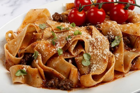 Pappardelle pasta with bolognese sauce, topped with parmesan cheese and cherry branch, homemade, no