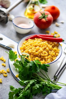 A vibrant image of uncooked chifferi rigati pasta in a white bowl, surrounded by fresh ingredients