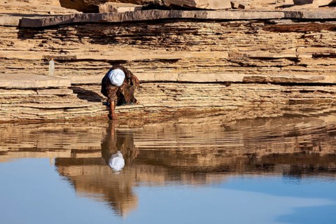 Individual person scooping water from a rock with a reflective surface, Tuareg collecting water in