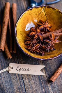 Top view of anise stars and cinnamon sticks in a textured yellow bowl on a wooden background,