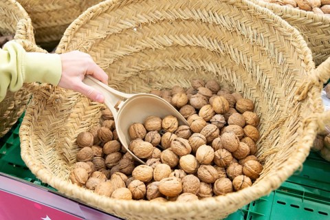 Cropped unrecognizable hands woman in a supermarket carefully selects fresh hazelnuts using a