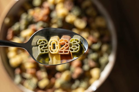 A spoonful of numerically shaped pasta displays the year 2026 above a bowl full of colorful number