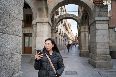 Asian female tourist exploring the historic medieval walls and ancient streets of Avila, Spain. She