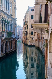 View from a gondola on a waterway in Venice going through the houses on a quiet and sunny morning