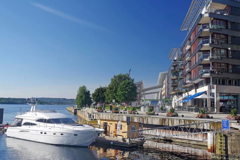 White yacht moored at dock next to modern buildings and clear blue sky, Oslo Fjord, Aker Brygge,