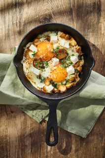 Fried eggs with spinach, mushrooms, grated cheese and feta cheese in small cast iron skillet. Top