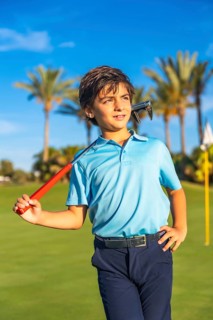 Vertical photo of a caucasian boy carrying a gold club along a course