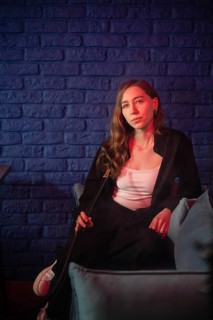 A woman sits in a dimly lit lounge, holding a hookah pipe against a blue brick wall. Red and blue