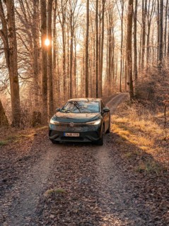 A car on a leafy forest path at sunset in autumn, car sharing, electric car, Volkswagen ID 5,