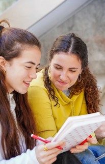 Two friends share a moment of study and collaboration, sitting closely while looking at a notebook