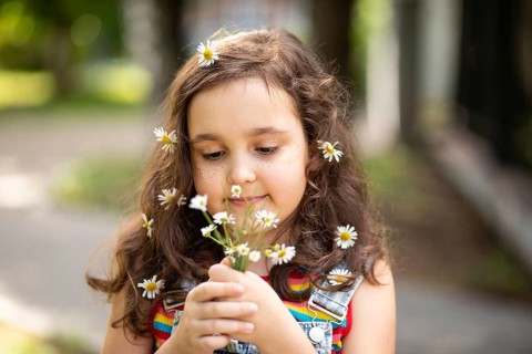 A joyful little girl in a rainbow-striped dress embraces the beauty of chamomile flowers. Her hair
