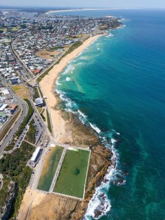 Image of a large ocean pool built along the rocky coastline of Newcastle, with golden beach, clear