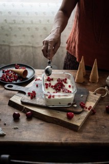 Cropped unrecognizable person scoops ice cream decorated with currants and gooseberries in a rustic