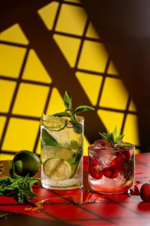 Two refreshing mojito cocktails displayed on a vibrant red surface with a bold yellow background.