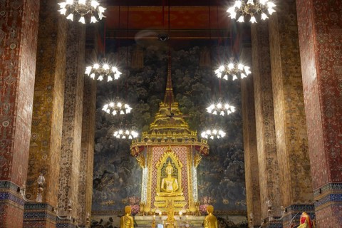Golden meditating Buddha surrounded by wall paintings with Buddhist teachings and representations