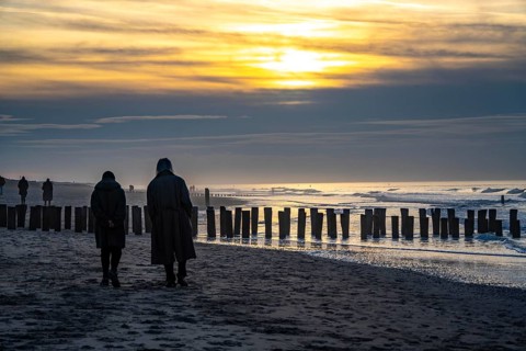 Winter on the North Sea, sunset at sea, beach walkers, coastal protection, through wooden posts,
