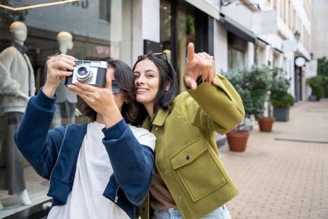 A lesbian couple enjoys a day out, capturing joyful photos with a vintage camera in an urban