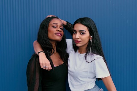 Two young friends pose against a blue background, showcasing friendship and happiness. One wears a